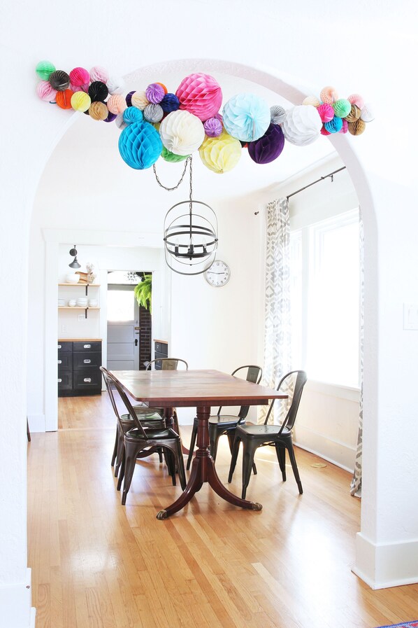 A dining area with a wooden table and chairs, a decorative paper ball garland, and a view into the kitchen.