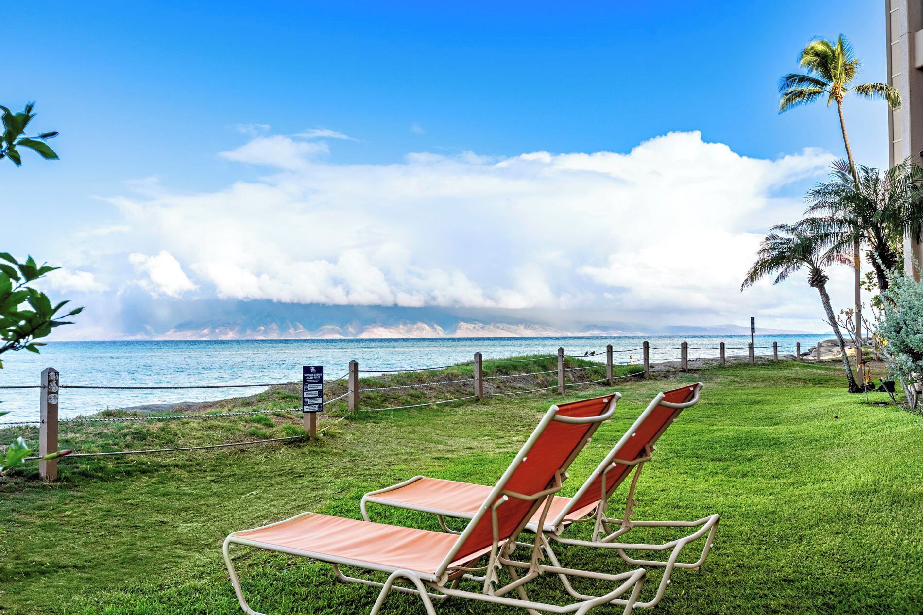 Ein Rasenbereich mit zwei Liegestühlen, die auf einen Strand zeigen.
