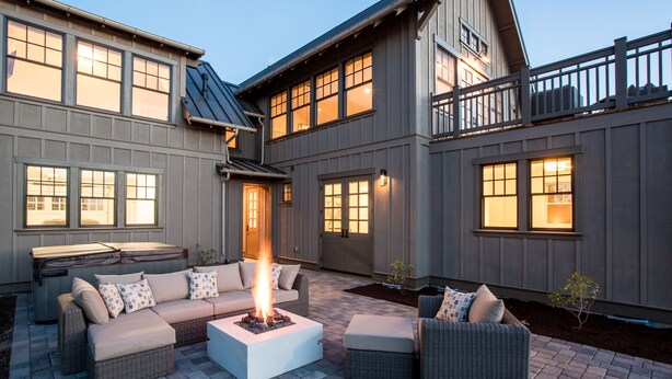 Een terras met buitenmeubilair, een vuurkorf, en een huis met meerdere ramen en een balkon.