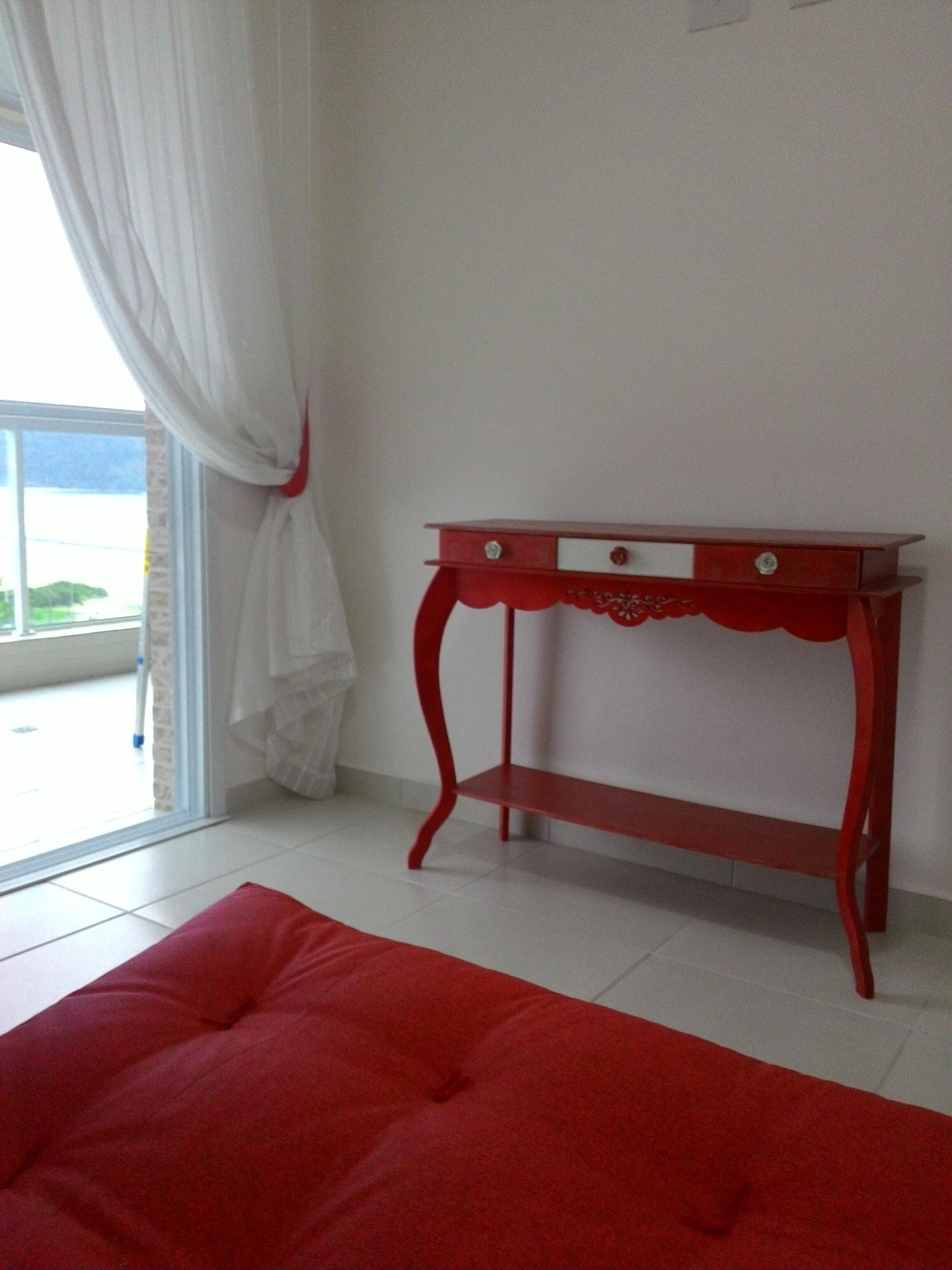 A room with a red sofa, a white and red table, and a view through a window with white curtains.