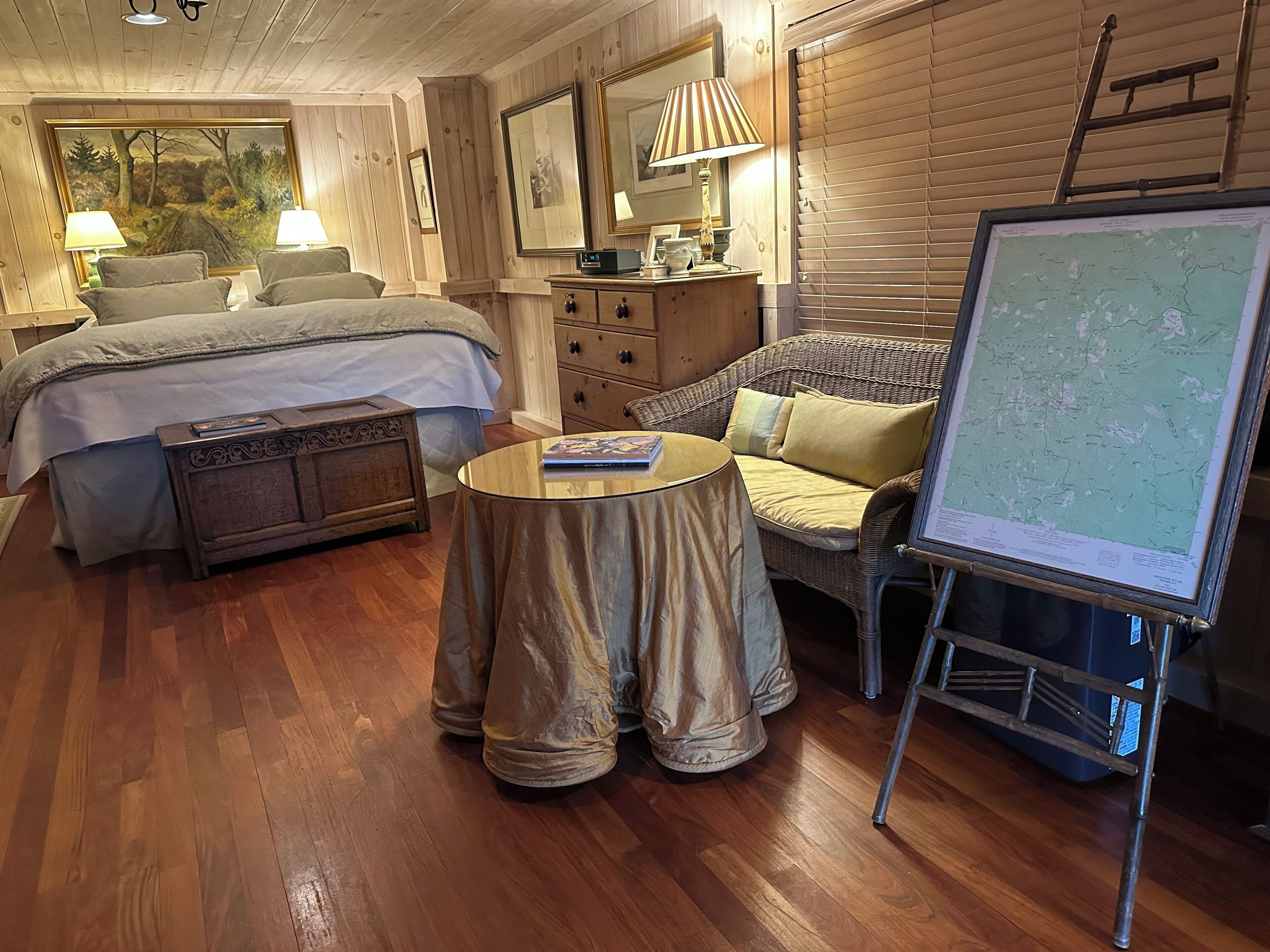 A cozy room with a bed, a sofa, a round table, and a map on a stand.