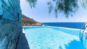 A clear blue pool with a stone wall and a view of the sea.