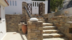A stone staircase leading to a white building with a rustic stone wall and a large terracotta pot.