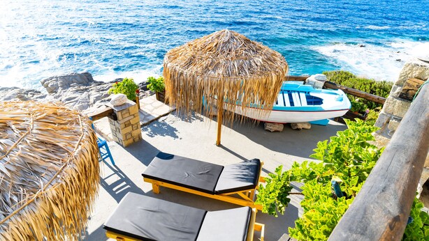 A beachside lounge with sun loungers, a thatched umbrella, and a boat.