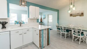 Une cuisine avec des meubles blancs, un îlot central en bois et des murs de couleur turquoise.