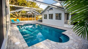 Une piscine entourée de parois en verre, une terrasse en bois et une maison ornée d’une fresque représentant un dauphin.