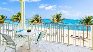 Een balkon met een tafel en stoelen, met uitzicht op een strand met palmbomen en de oceaan.