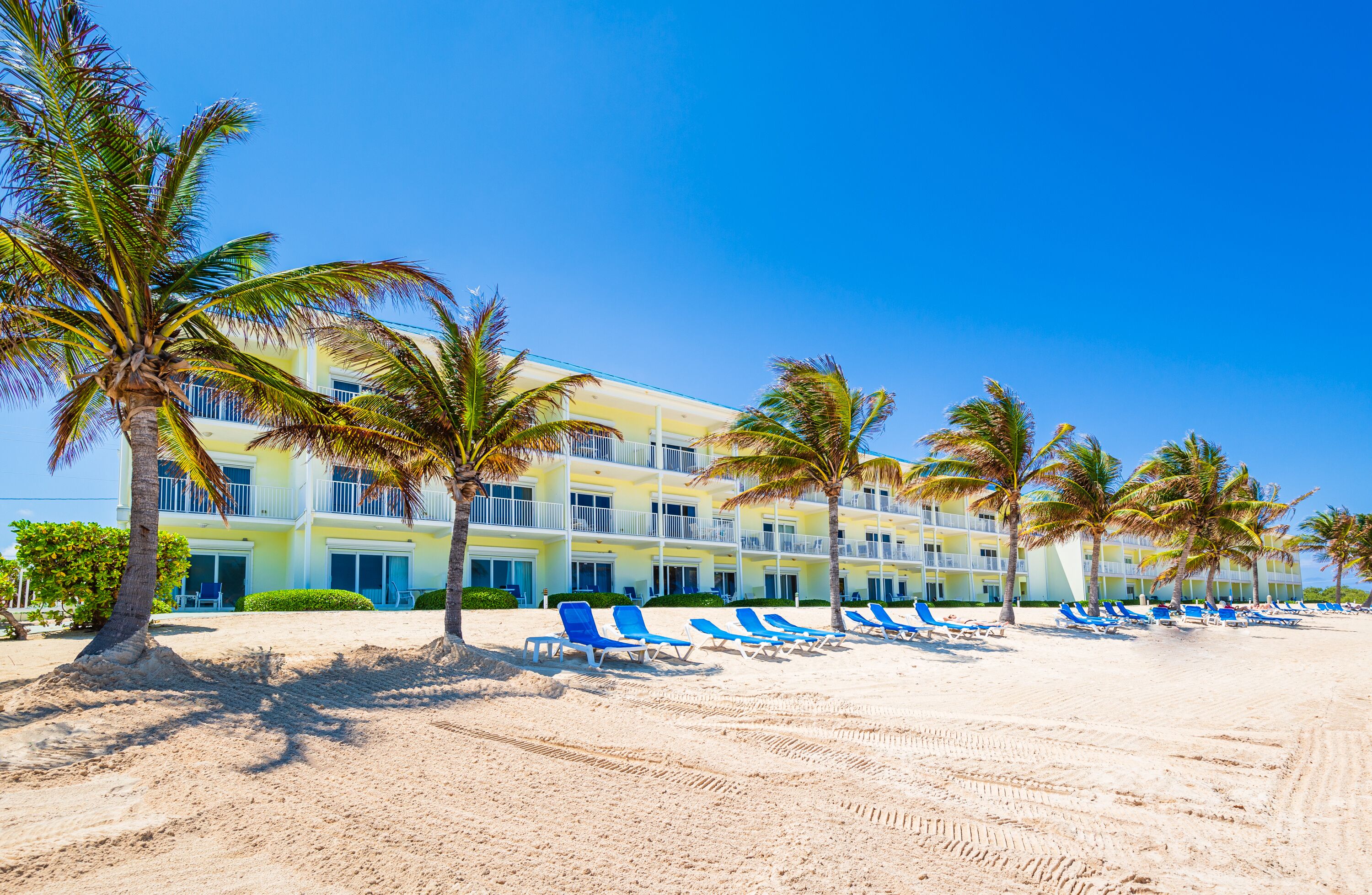 A beachfront hotel with multiple balconies, a sandy beach, and palm trees.