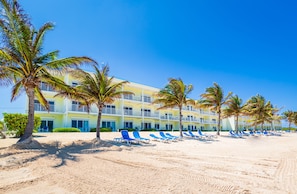 A beachfront hotel with multiple balconies, a sandy beach, and palm trees.