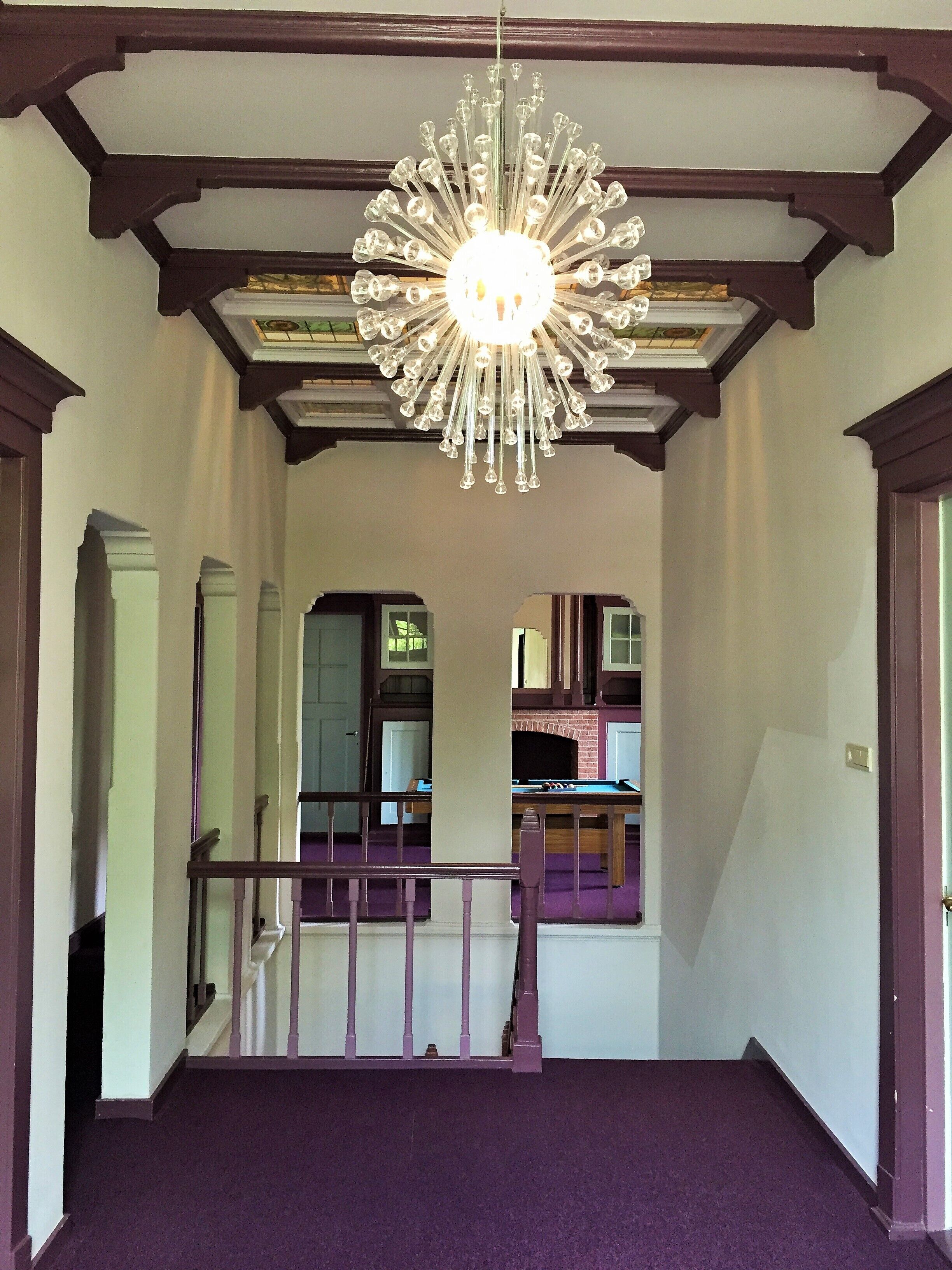 A grand hallway with a large chandelier, wooden beams, and a purple carpet.