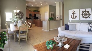 A spacious living room with a white sofa, wooden coffee table, and a dining area with a wooden table and chairs. - •Townhome with Direct Beach Access •Sleeps 10 •4BR 3BA •Steps to Flagler Ave (New Smyrna Beach)