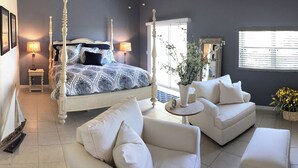 A bedroom with a four-poster bed, a white sofa, a coffee table, and a television. - •Townhome with Direct Beach Access •Sleeps 10 •4BR 3BA •Steps to Flagler Ave (New Smyrna Beach)