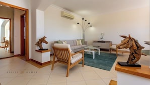 Een moderne woonkamer met een bank, fauteuils, een salontafel en decoratieve houten sculpturen.