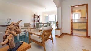 Een moderne woonkamer met een houten salontafel, een bank en een eethoek met stoelen. Een keuken is zichtbaar door een open deur.