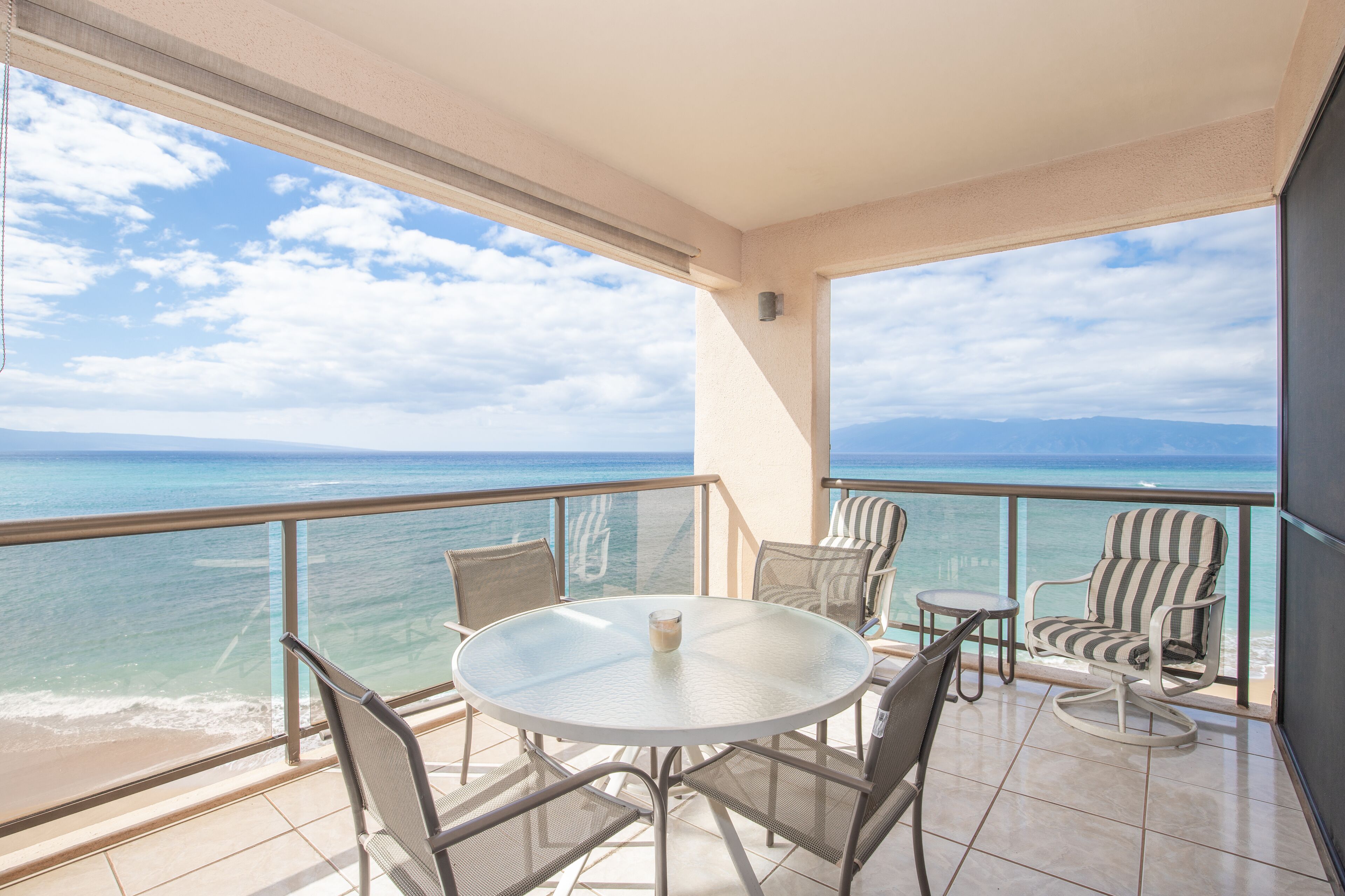 A balcony with a round table and chairs, overlooking a beach and ocean.