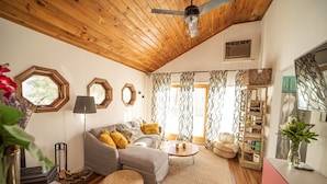 Una sala de estar acogedora con techo de madera, un sofá con cojines amarillos, una mesita de centro y una estantería.