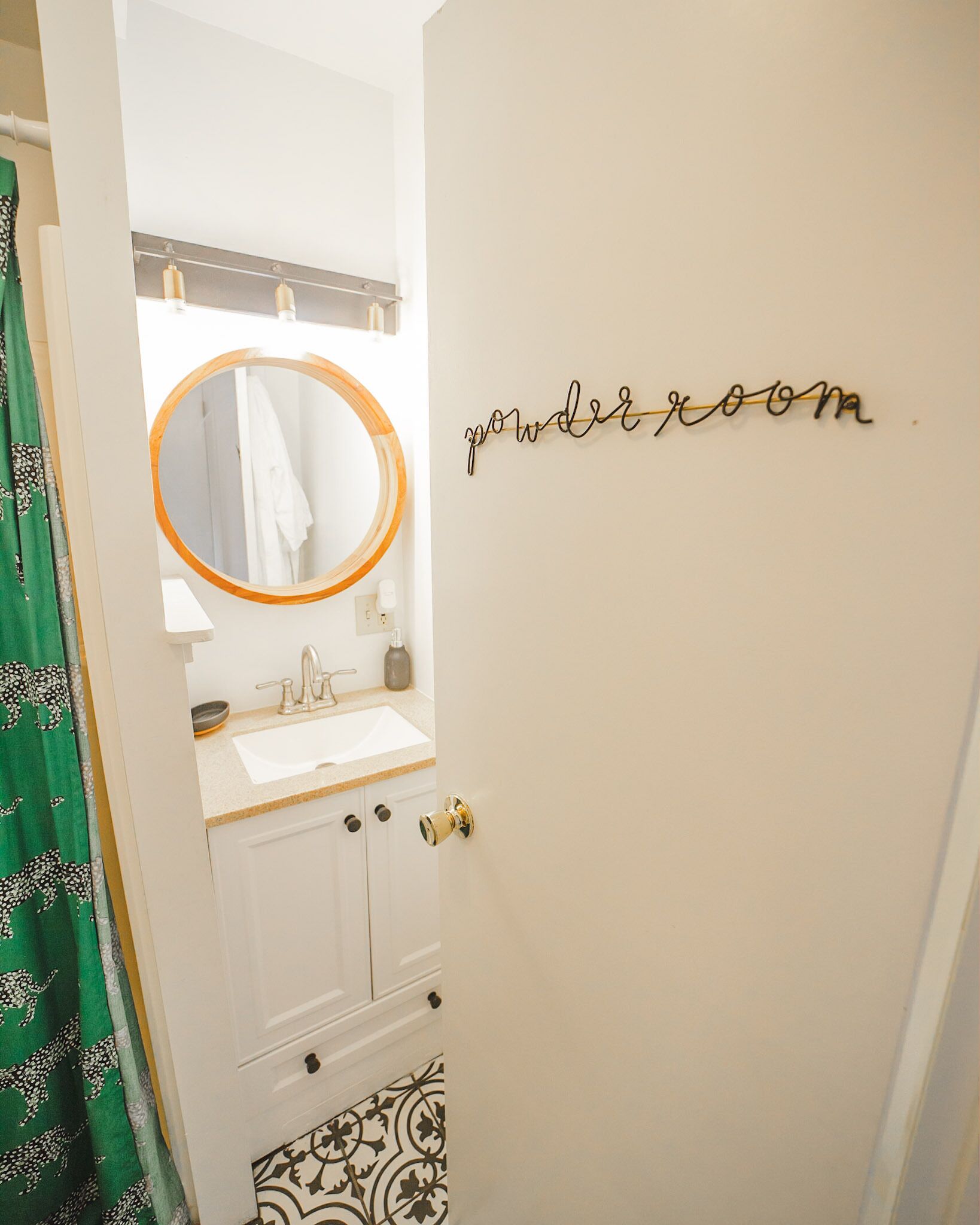 Een badkamer met een wit wastafel, een spiegel met houten lijst, en een deur met het bordje 'powder room'.