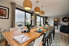 Ein moderner Essbereich mit einem langen Holztisch, mehreren Stühlen und Pendelleuchten.