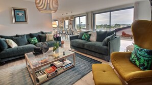 Ein modernes Wohnzimmer mit zwei Sofas, einem Couchtisch und einem gelben Sessel. Im Hintergrund ist eine Essecke mit Tisch und Stühlen zu sehen.