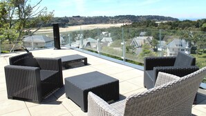 Eine Terrasse mit Korbmöbeln, einer Glastrennwand und Blick auf eine Wohngegend.