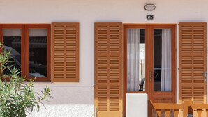 A building with three wooden doors and windows, a white exterior, and a small balcony with a plant.