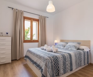 Een slaapkamer met een groot bed, twee nachtkastjes met lampen, een dressoir, een raam met gordijnen en een plafondlamp.