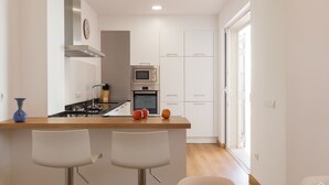 A modern kitchen with white cabinets, a central island with bar stools, a microwave, and a stove.