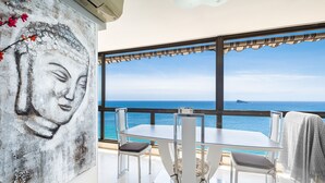 A dining area with a table and chairs, a Buddha painting on the wall, and a view of the sea. - Los Gemelos 21-B (Benidorm)