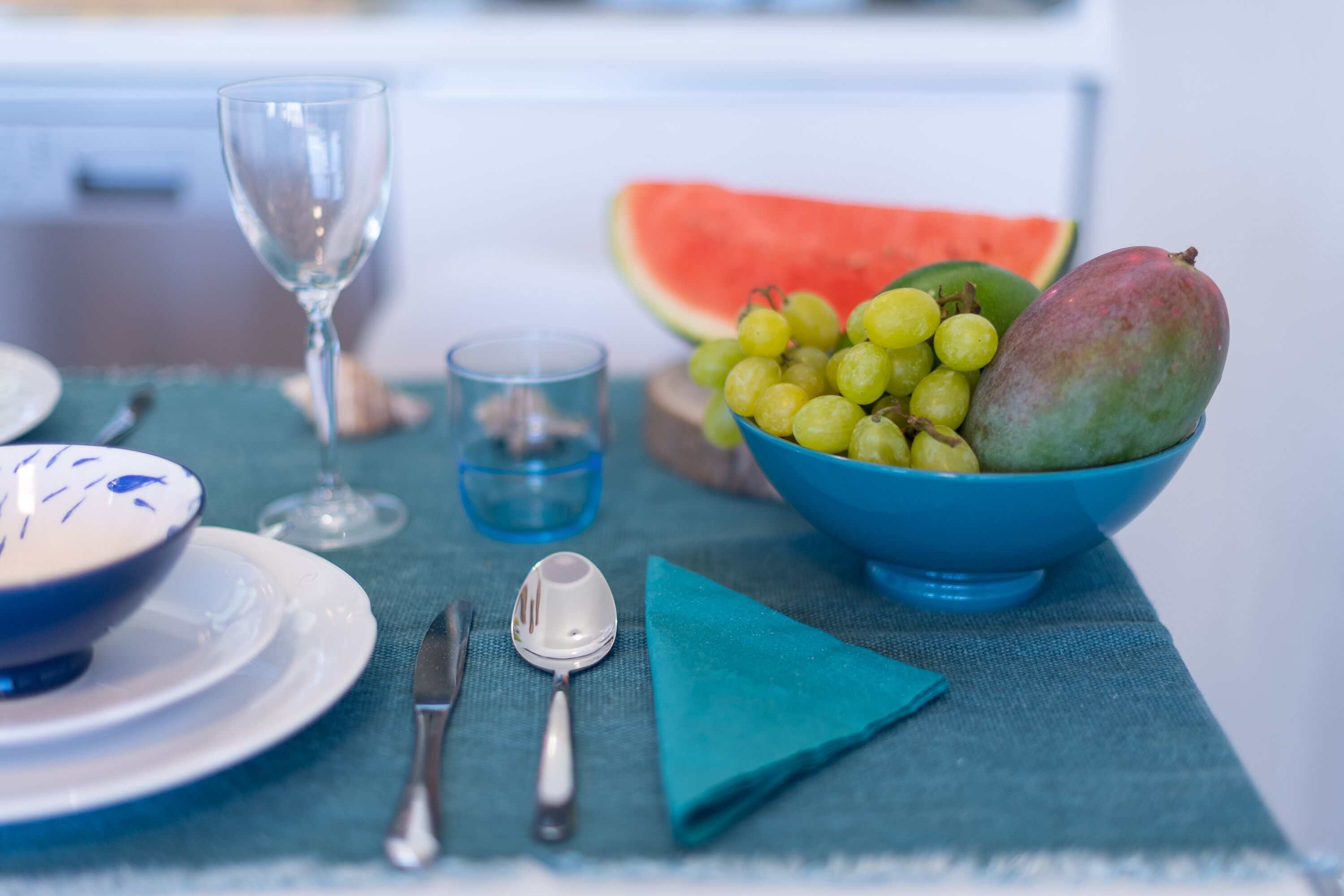 A table set with a blue bowl of fruit, a glass of water, a plate, and cutlery.
