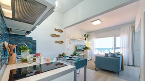Ett modernt kök med en köksö i mitten, en matplats med en blå soffa och utsikt över havet.