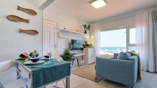 Ett modernt vardagsrum med en matplats, en soffa, en tv och utsikt över havet.