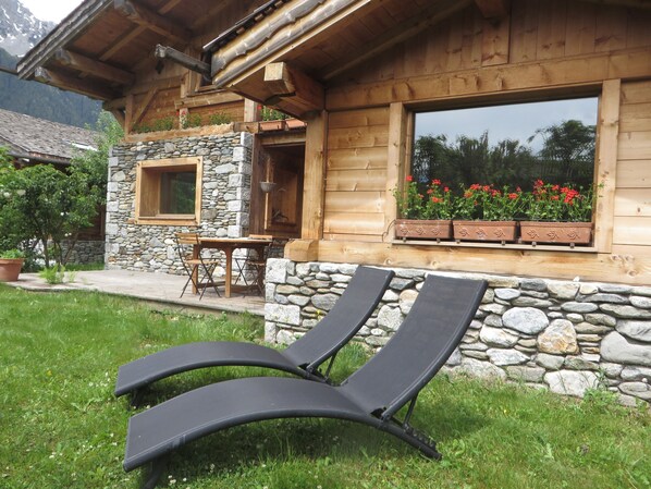 Eine Holzhütte mit Steinmauern, einer Holzdiele und zwei Liegestühlen.