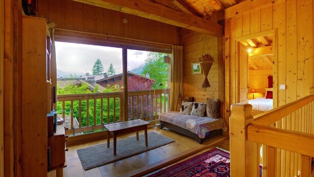 Interior de una cabaña de madera con balcón, un sofá y una planta colgante.