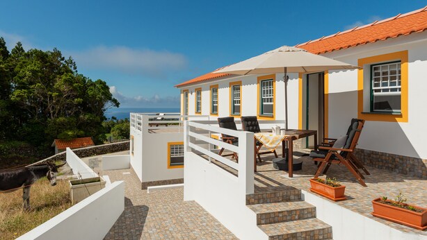 Un bâtiment blanc orné de bordures orange et surmonté d’un toit en tuiles, avec une terrasse aménagée avec des meubles d’extérieur et des plantes en pot.