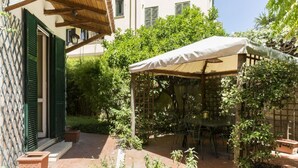 Un pati amb una taula i caires, envoltat de plantes en testos i una pèrgola amb un tendal blanc.