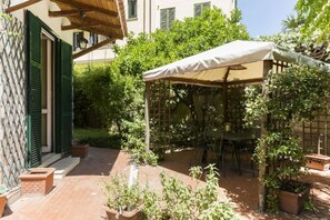 A patio with a table and chairs, surrounded by potted plants and a pergola with a white canopy.