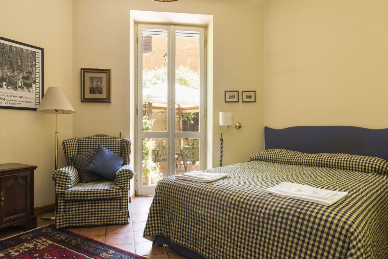 A bedroom with a checkered bedspread, a chair with a pillow, a lamp, and a framed picture on the wall.