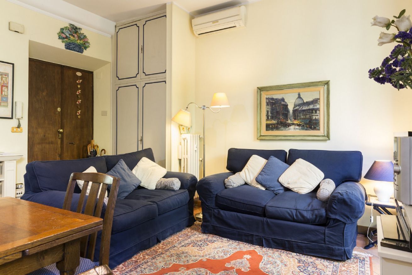 Een woonkamer met twee blauwe banken, een houten eettafel en een vloerkleed met een patroon.