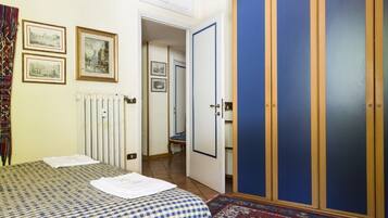Une chambre avec une couvre-lit à carreaux, un radiateur, des tableaux encadrés accrochés au mur, une armoire bleue et un tapis à motifs.