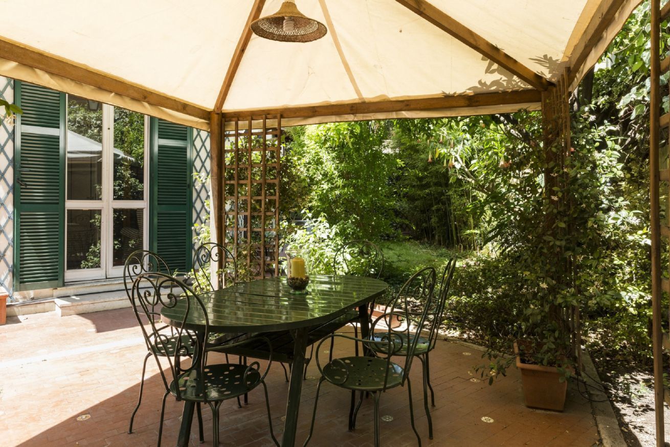 Une terrasse couverte, dotée d’une table et de chaises, et entourée de verdure.
