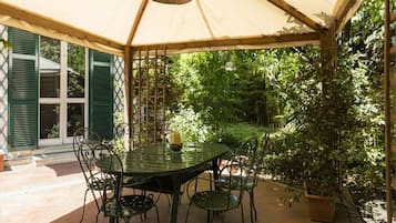 Une terrasse couverte, dotée d’une table et de chaises, et entourée de verdure.