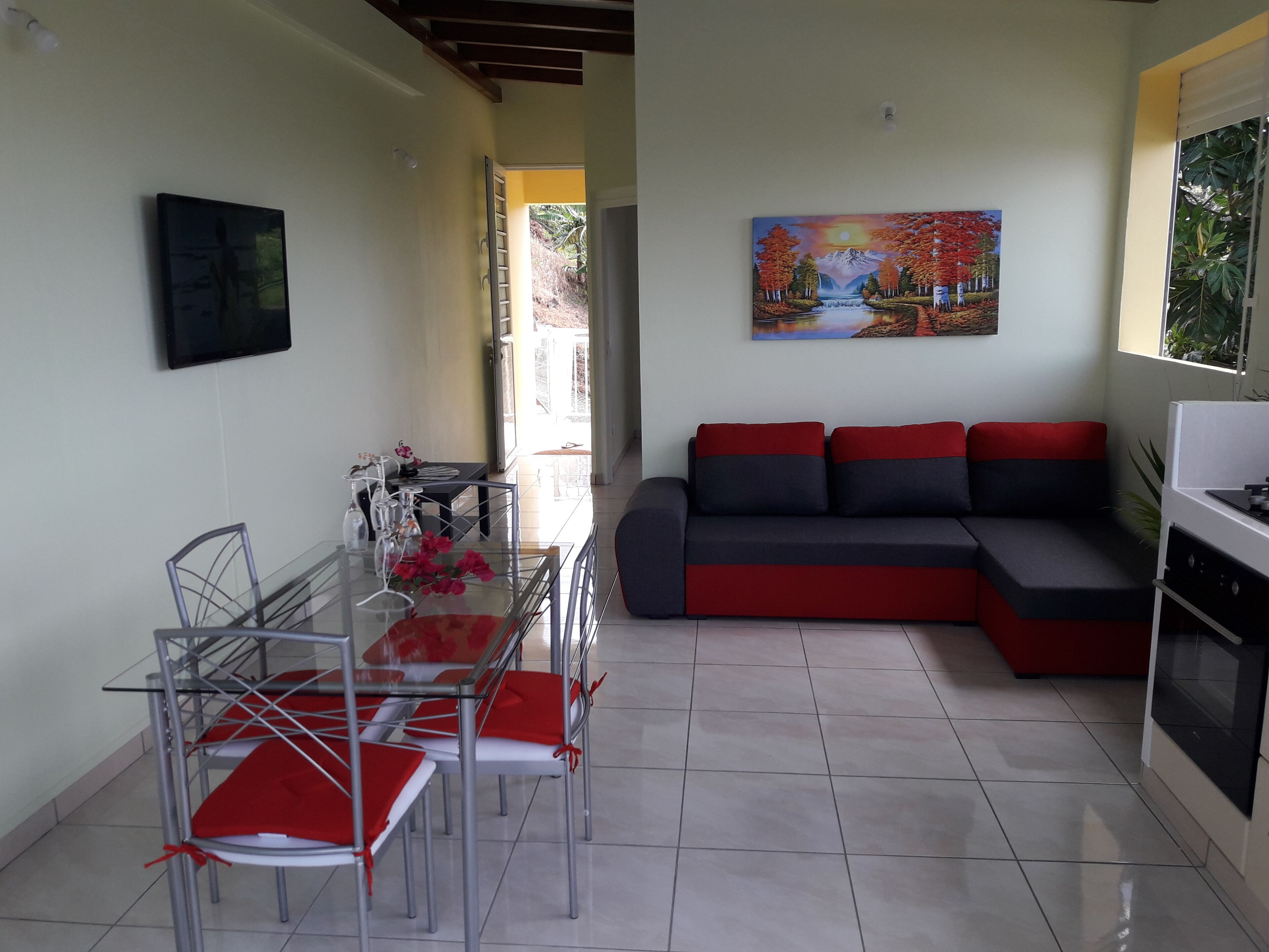 Un soggiorno moderno con un tavolo da pranzo in vetro, un divano rosso e nero e un quadro appeso al muro.