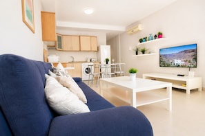 En stue med sofa, sofabord, TV, et tekøkken og et spisebord.