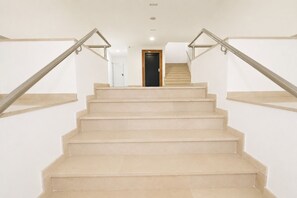 Una escalera con peldaños color beige y barandas de metal que conduce a una puerta en la parte superior.