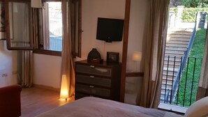 A bedroom with a bed, a dresser, a TV on the wall, and a balcony with a railing.