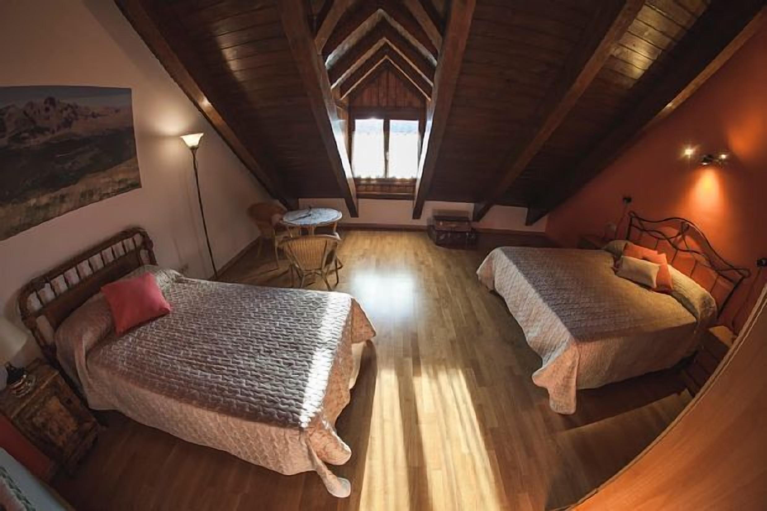 Un dormitorio acogedor en el ático con dos camas, una mesita y un cuadro en la pared.