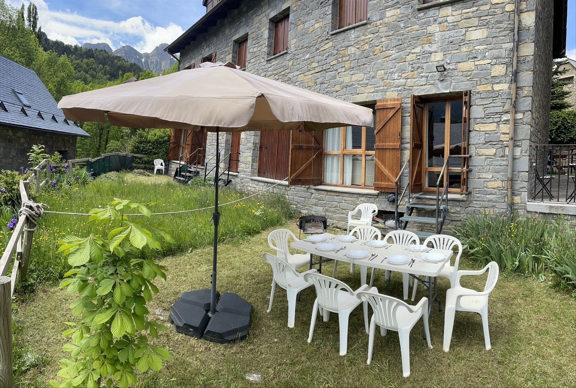 Un bâtiment en pierre doté d’un espace repas comprenant une table, des chaises, un parasol et un barbecue.