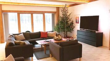 Ein gemütliches Wohnzimmer mit einem Ecksofa, einem Couchtisch, einer kleinen Weihnachtstanne und einem Fernseher auf einem Schrank.