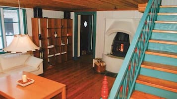 A wooden-floored living room with a staircase, a fireplace, and a bookshelf.