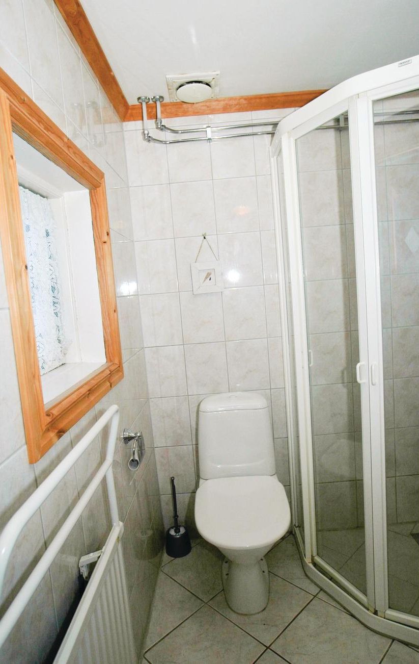 A bathroom with a toilet, a shower enclosure, and a window with a wooden frame.